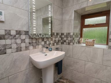 A bathroom with a white pedestal sink a mirror with lights on tiles and a window with a basket at Gelli Barn Near Llandeilo