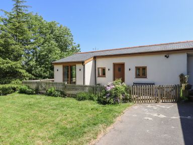 A small house with wooden doors and windows and a fenced garden with grass and plants at Adipit Stables Buckland Brewer near Bideford