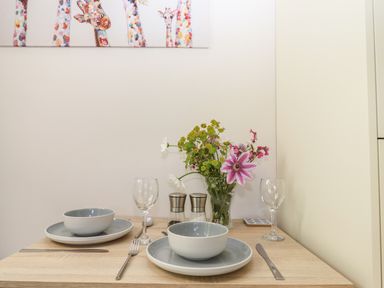 A small dining table set with bowls plates cutlery glasses and a vase of flowers at Adipit Stables Buckland Brewer near Bideford