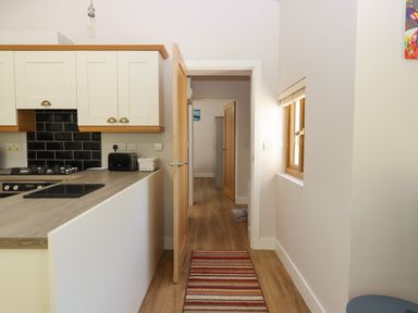 A kitchen area with cabinets a countertop and a door leading to a hallway with wooden flooring and a striped rug at Adipit Stables Buckland Brewer near Bideford
