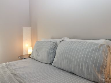 A bedroom with two gray striped pillows on a bed next to a small table and a lit floor lamp at Adipit Stables in Buckland Brewer near Bideford