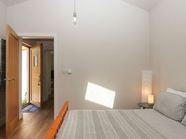 A bedroom with bed and bedside table with lamps near an open wooden door at Adipit Stables in Buckland Brewer near Bideford