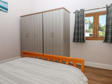 A bedroom with a wooden bed frame a gray wardrobe and a window with curtains at Adipit Stables in Buckland Brewer near Bideford