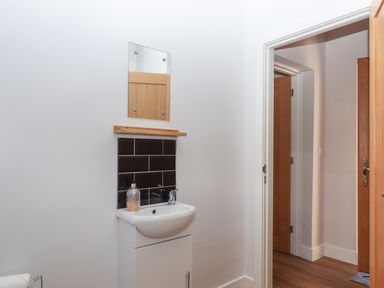 A small bathroom with a white sink and cabinet a mirror and black tile backsplash seen at Adipit Stables in Buckland Brewer near Bideford