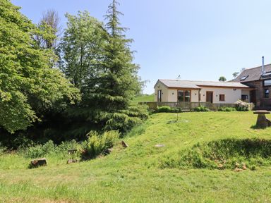 A house with a fenced garden surrounded by grass and trees at Adipit Stables in Buckland Brewer near Bideford