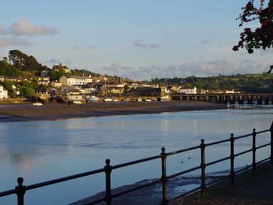 A riverside view with boats docked near houses and a bridge in the distance at Adipit Stables in Buckland Brewer near Bideford