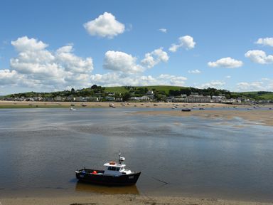 A small boat anchored near a sandy shore with houses and green hills in the background at Adipit Stables in Buckland Brewer near Bideford