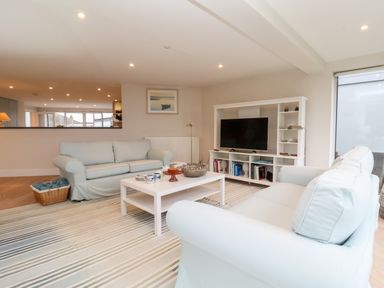 A living room with two sofas a white coffee table a striped rug and a TV unit at Pebbles in Southwold