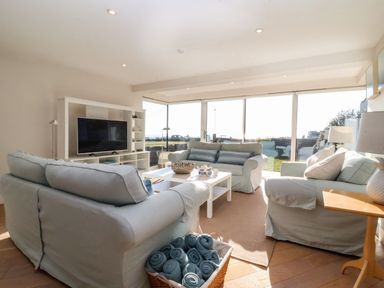 A living room with sofas a coffee table a television and large windows overlooking a garden at Pebbles in Southwold