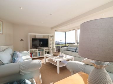 A living room with sofas a coffee table a TV and large windows overlooking the sea at Pebbles in Southwold