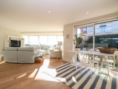 A living room with sofas a television and a table with transparent chairs at Pebbles in Southwold