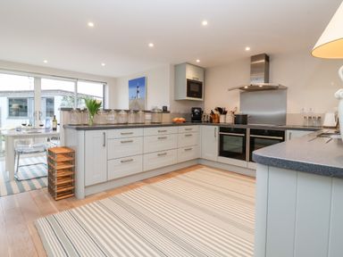 A kitchen with white cabinets a striped rug and a dining table with glasses of wine at Pebbles in Southwold