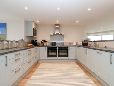 A kitchen with white cabinets gray countertops double oven and striped rug at Pebbles in Southwold