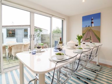 A dining room with a set table and glass doors leading to an outdoor patio at Pebbles in Southwold