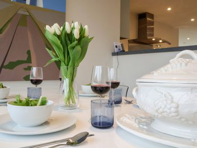 A dining table set with white bowls of salad wine glasses a vase of white tulips and a ceramic tureen in a modern kitchen at Pebbles Southwold