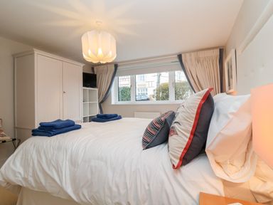 A bedroom with a bed with pillows and folded towels near a window with curtains and a wardrobe at Pebbles in Southwold