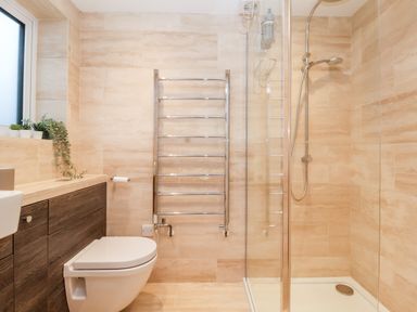 A bathroom with a toilet a wooden cabinet a towel rack and a glass-enclosed shower at Pebbles in Southwold