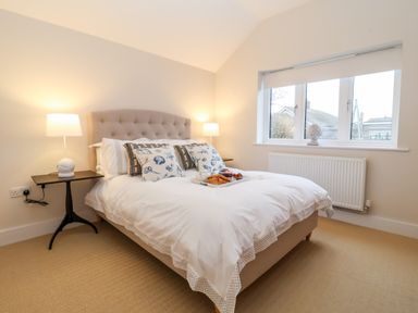 A bedroom with a bed with patterned pillows and a tray of food a window and bedside tables with lamps at Pebbles in Southwold