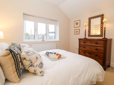 A bedroom with a bed with patterned pillows a wooden chest of drawers with a mirror and lamps at Pebbles in Southwold
