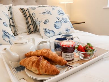 A tray with croissants jam strawberries a teapot and cups on a bed with seashell patterned pillows at Pebbles in Southwold
