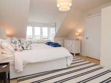 A bedroom with a double bed pillows folded towels striped rug and a white chest of drawers at Pebbles in Southwold