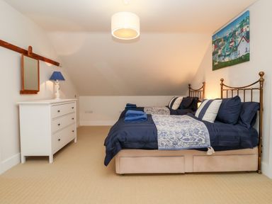 A bedroom with two single beds blue bedding white dresser with lamp and wall mirror at Pebbles in Southwold