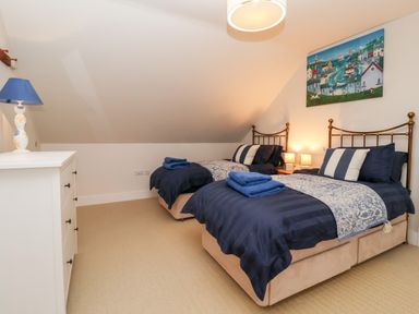 A bedroom with two twin beds with blue bedding a white dresser with a blue lamp and a painting on the wall at Pebbles in Southwold