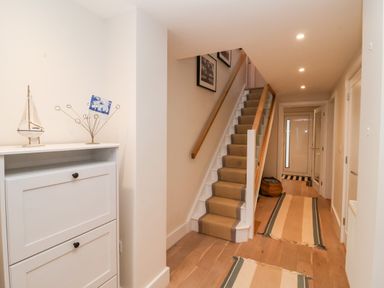 A hallway with stairs and a white cabinet with decorative items at Pebbles in Southwold