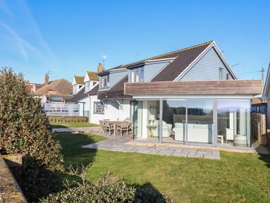 A house with large glass windows and a patio with outdoor furniture and a lawn at Pebbles in Southwold