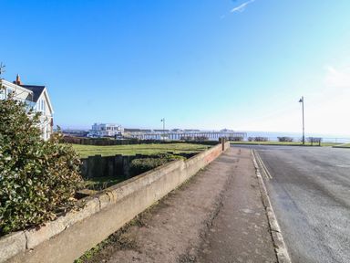 A street leading to a pier over the water with grassy areas and houses on the left at Pebbles in Southwold