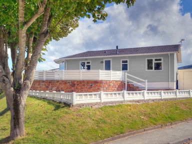 A house with a white fence on a grassy slope and a tree in front at E19 The Warren in Abersoch