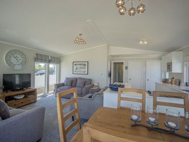An open plan living room and kitchen with wooden dining table and chairs and sofas at E19 The Warren in Abersoch