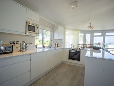 A kitchen with white cabinets a microwave toaster kettle oven and dining table at E19 The Warren in Abersoch
