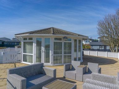 An outdoor patio area with wicker seating and a circular building with large windows at E19 The Warren in Abersoch