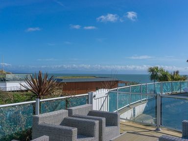 A patio with wicker chairs and glass railing overlooking the sea at E19 The Warren in Abersoch