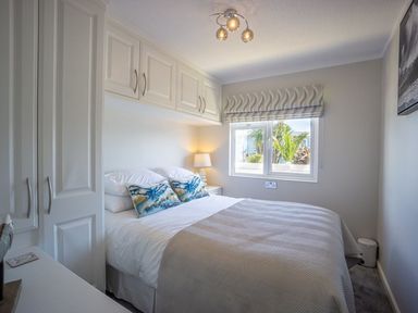 A bedroom with a bed pillows bedside lamp window and built in cupboards at E19 The Warren in Abersoch