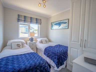 A bedroom with two single beds blue blankets a window and a whale painting at E19 The Warren in Abersoch