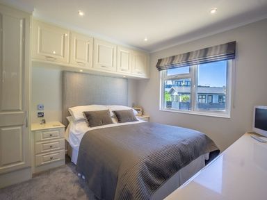 A bedroom with a double bed under fitted cabinets and a window with a view at E19 The Warren in Abersoch