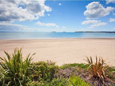 A sandy beach with plants in the foreground and calm sea with islands in the distance at E19 The Warren in Abersoch