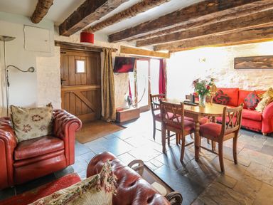 A living room with wooden beams a wooden door a dining table with chairs and red sofas at Ty Fferm Hen in Talybont-on-Usk
