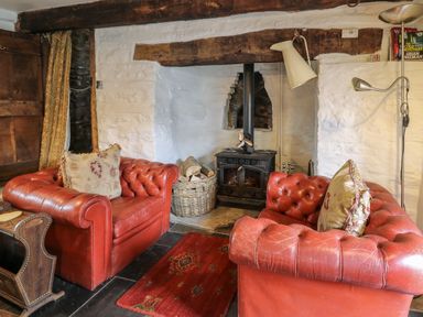 A living room with red leather armchairs a wood burning stove and a rug at Ty Fferm Hen in Talybont-on-Usk