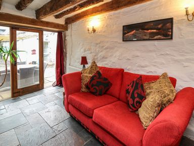 A living room with a red sofa and cushions a floor lamp and glass door leading outside at Ty Fferm Hen in Talybont-on-Usk