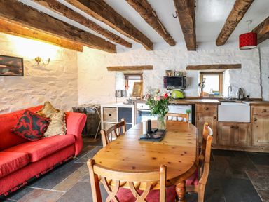 A kitchen dining area with a wooden table and chairs a red sofa wooden beams on ceiling and white stone walls at Ty Fferm Hen in Talybont-on-Usk