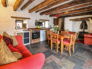 A rustic living area with wooden beams a red sofa a wooden dining table with chairs and a small kitchen at Ty  Fferm Hen in Talybont-on-Usk