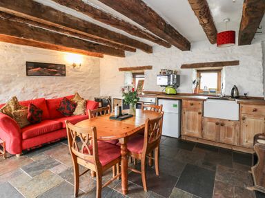 A kitchen and dining area with a wooden table and chairs a red sofa and kitchen appliances at Ty Fferm Hen in Talybont-on-Usk