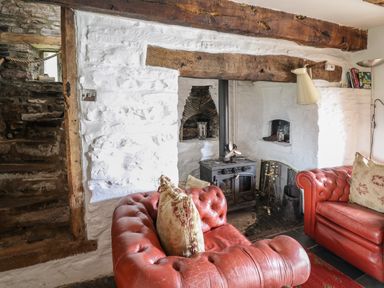 A living room with red leather sofas a wood burning stove and white painted stone walls at Ty Fferm Hen in Talybont-on-Usk