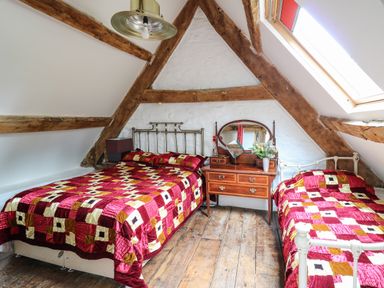 A bedroom with two beds one double and one single with red patterned quilts and a wooden dresser under exposed wooden beams at Ty  Fferm Hen in Talybont-on-Usk
