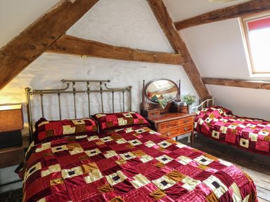 A bedroom with two beds a wooden dresser with mirror and wooden beams on the ceiling at Ty Fferm Hen in Talybont-on-Usk