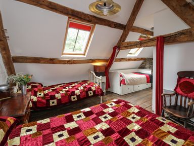 A bedroom with three beds a wooden chair and visible ceiling beams at Ty Fferm Hen in Talybont-on-Usk