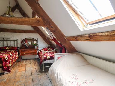 An attic bedroom with three beds wooden beams a dresser with a mirror and a skylight at Ty Fferm Hen in Talybont-on-Usk